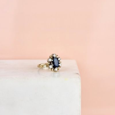 a blue sapphire and diamond cluster ring on a white marble block