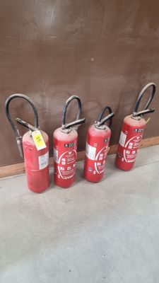 Quatre extincteurs sont alignés contre un mur