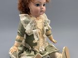 an image of a doll sitting on the ground wearing a green dress