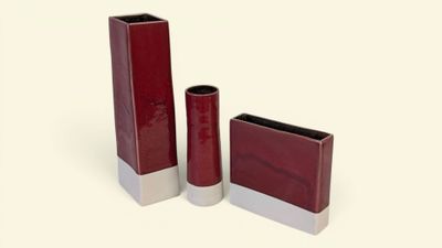 trois vases rouges posés les uns à côté des autres sur une surface blanche