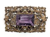 un gros plan sur une broche composée d'une pierre violette et d'une perle