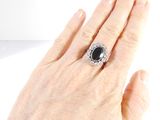 a woman ' s hand holding a ring with a black stone on it