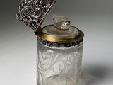 an antique silver and glass jar with a lid on a white surface