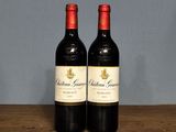 two bottles of red wine sitting on top of a wooden table