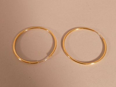 two pairs of gold hoop earrings sitting on top of a white surface