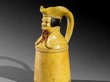 une vieille cruche jaune ornée d'une tête d'homme coiffée d'un chapeau