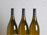 three bottles of wine sitting on a wooden table next to a bottle of wine
