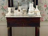 une table sur laquelle sont posés un miroir et des tasses, devant un mur recouvert de papier peint