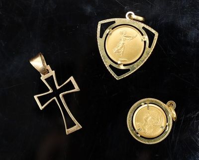trois pendentifs en or représentant une croix et une médaille, sur un fond noir