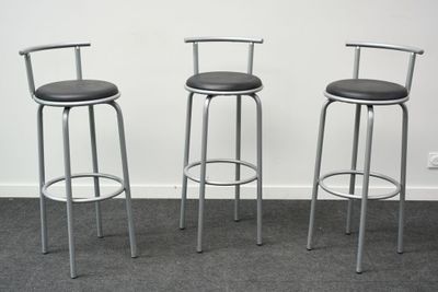 trois tabourets en métal placés les uns à côté des autres sur un sol recouvert de moquette