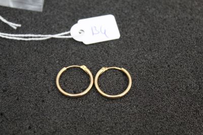 two pairs of gold hoop earrings on a black surface with a price tag