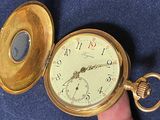 someone is holding a gold pocket watch in their hand on a blue surface