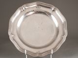 un plat ancien en argent posé sur un socle, sur fond gris