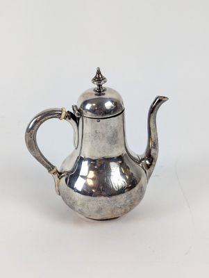 une théière ancienne en argent avec un couvercle, posée sur une surface blanche