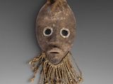 a wooden mask with long hair and eyes on a gray background