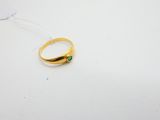 une bague en or sertie d'une pierre verte repose sur une surface blanche