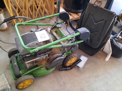 a green lawn mower sitting on the floor next to a trash can