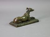 bronze statue of a dog laying on a rock on a white surface