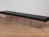 un banc noir posé sur un parquet, devant un mur blanc