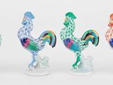 quatre figurines de coqs aux couleurs vives sont alignées sur une surface blanche