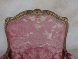 a pink chair with a gold frame and a white wall behind it