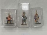 three miniature figurines of knights in plastic containers on a white surface