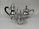 three pieces of silver tea and coffee set on a white surface