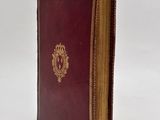 an old book with a red cover sitting on a white surface