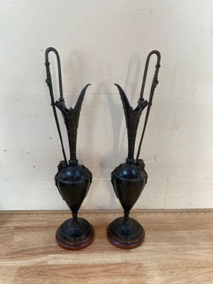 deux vases noirs posés sur une table en bois, avec un mur blanc en arrière-plan
