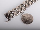 silver chain bracelet with a coin on a white surface