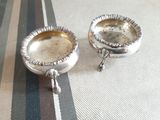 two silver dishes sitting on a striped table cloth