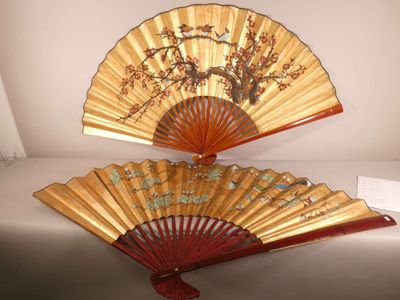 une paire d'éventails orientaux ornés de fleurs et d'oiseaux, posés sur une table