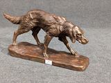 statue en bronze représentant un chien, posée sur un socle en bois, sur fond gris
