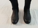 the black boots are lined up on the bed with a white sheet