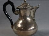 an antique silver tea pot with a black handle sitting on a table