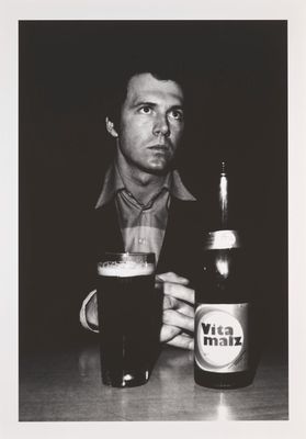 une photo en noir et blanc d'un homme assis à une table avec une bière