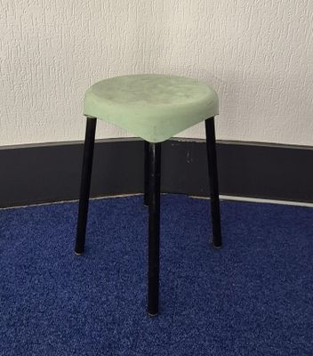 a green stool sitting on a blue carpet in front of a white wall