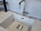 a white sink in a kitchen with a wooden shelf above it