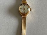 a gold wrist watch with a white face on a white surface