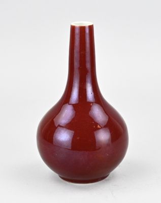 un vase rouge posé sur une surface blanche