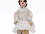 doll sitting on a white surface wearing a white dress and brown shoes