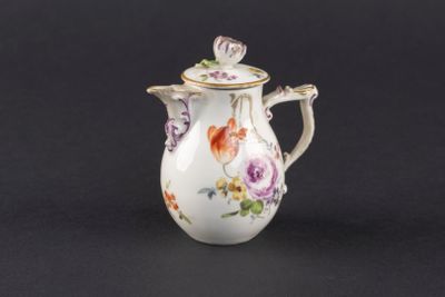 un petit vase blanc orné de fleurs, posé sur un fond noir