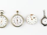 four different types of pocket watches are displayed on a white surface