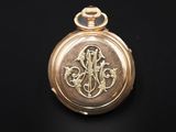 an image of a gold pocket watch with a monogram on it