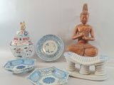 a statue of buddha sitting on a pedestal next to a bowl and plates