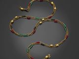 un collier composé de perles dorées, émeraude et rouges sur fond noir