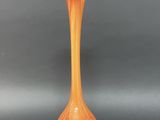 an orange and yellow vase sitting on top of a black table