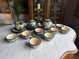 many cups and saucers on a table with a vase in the background