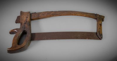 une vieille scie à main en bois avec un manche en bois, posée sur une surface blanche