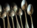 six cuillères en argent sont alignées les unes à côté des autres sur un fond noir